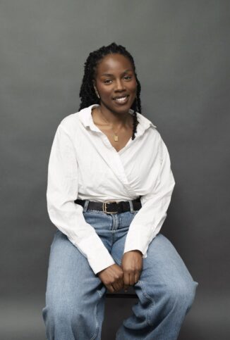 Studio portrait of Amara O smiling in white shirt and jeans