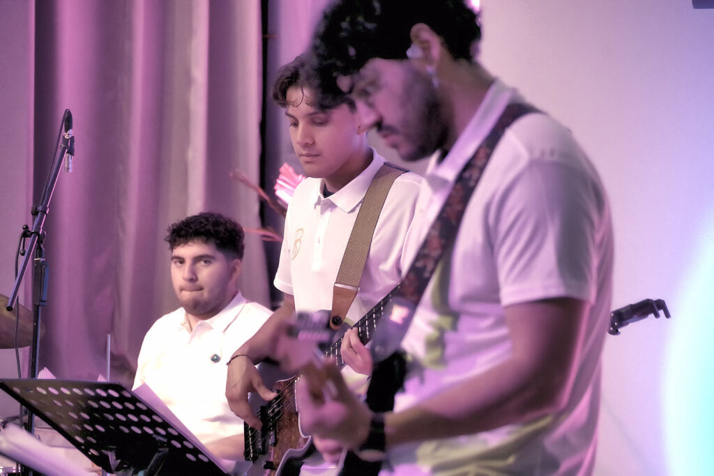 Youth worship band performing under purple stage lights, drummer and guitarists in white polos.