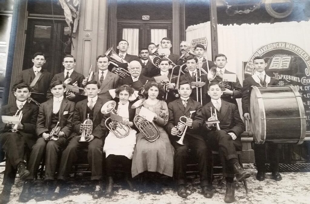 Circa 1910 group portrait of a Russian mission brass band with instruments outside a storefront.