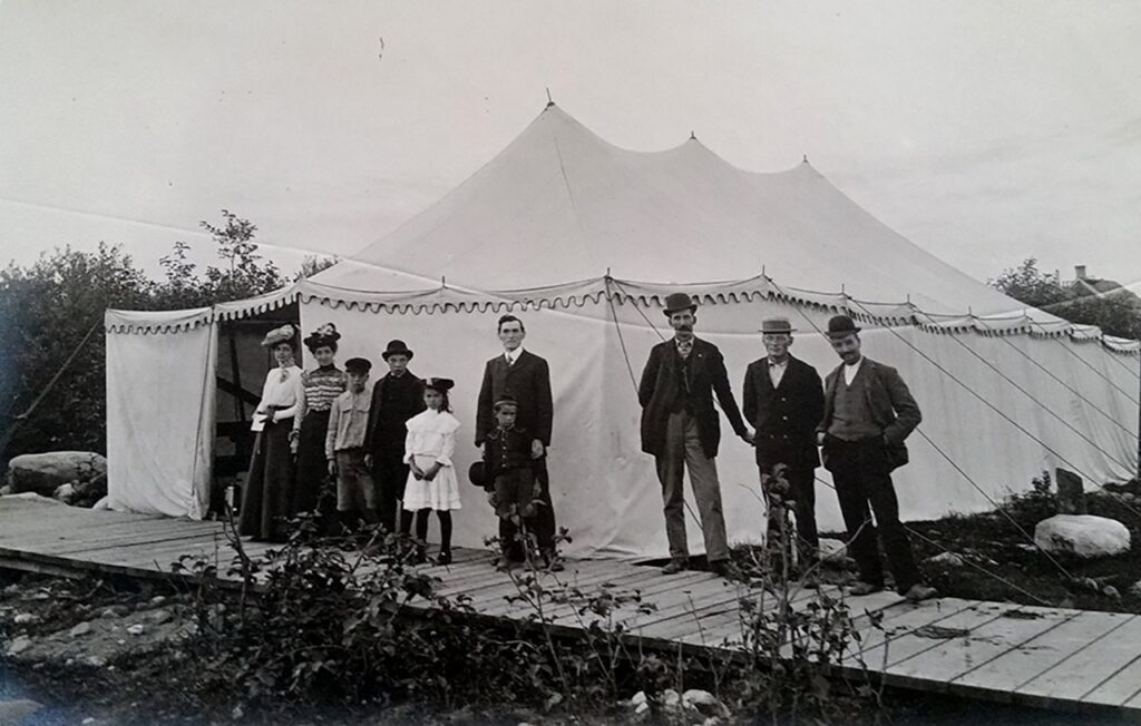 Vintage photo of a group of adults and children posed on a boardwalk before a large canvas tent.