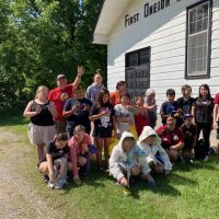 Group of kids and adults posing outside a white building on a sunny day.
